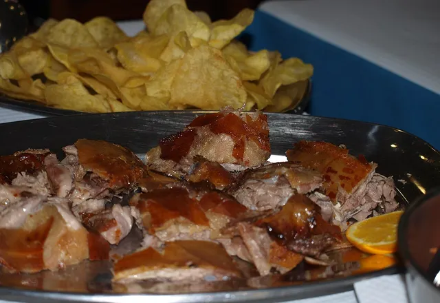 Prato de leitão assado às postas, com batata frita e rodela de laranja