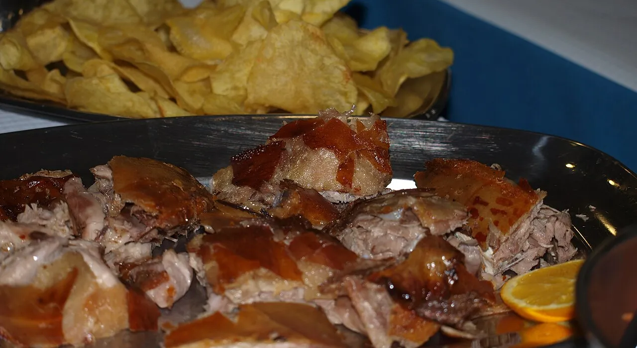 Prato de leitão assado às postas, com batata frita e rodela de laranja
